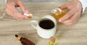 CBD energy tincture being added to a morning cup of black coffee with dropper bottles on a wooden table.