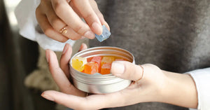Hands holding white tin filled with colorful CBD food products and gummy candies