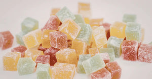 CBD gummies in assorted yellow, green, and red sugar-coated cubes piled on a soft white background.