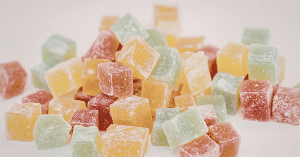 CBD gummies in assorted yellow, green, and red sugar-coated cubes piled on a soft white background.