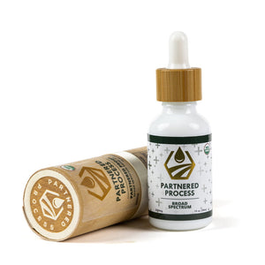 Partnered Process broad spectrum hemp oil tincture bottle with bamboo dropper beside its cardboard tube packaging.