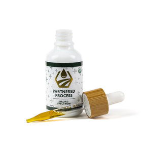 Open Partnered Process broad spectrum hemp oil tincture bottle with bamboo dropper showing golden hemp extract.