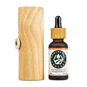 Partnered Process Partnered Pet hemp oil tincture bottle next to its wooden cylinder packaging.