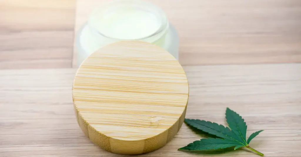 CBD topical cream jar with bamboo lid and cannabis leaf on wooden table
