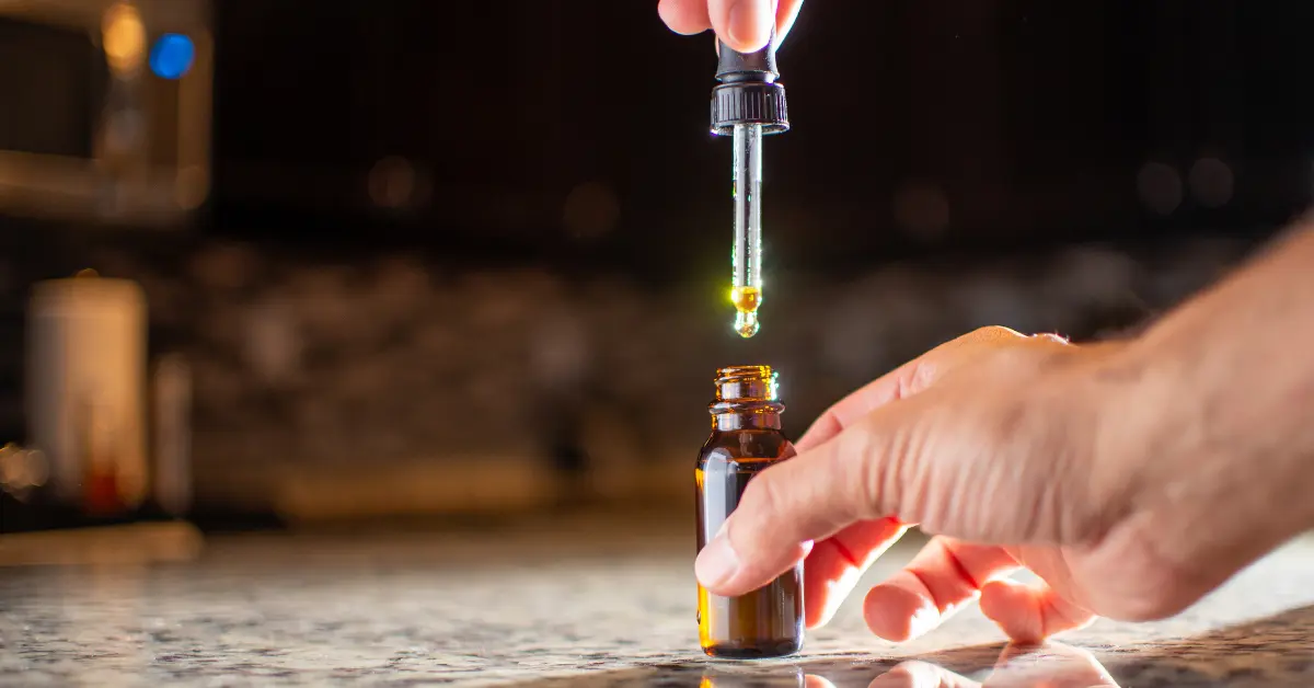 Broad-spectrum CBD being dropped into an amber glass bottle on a reflective kitchen surface.
