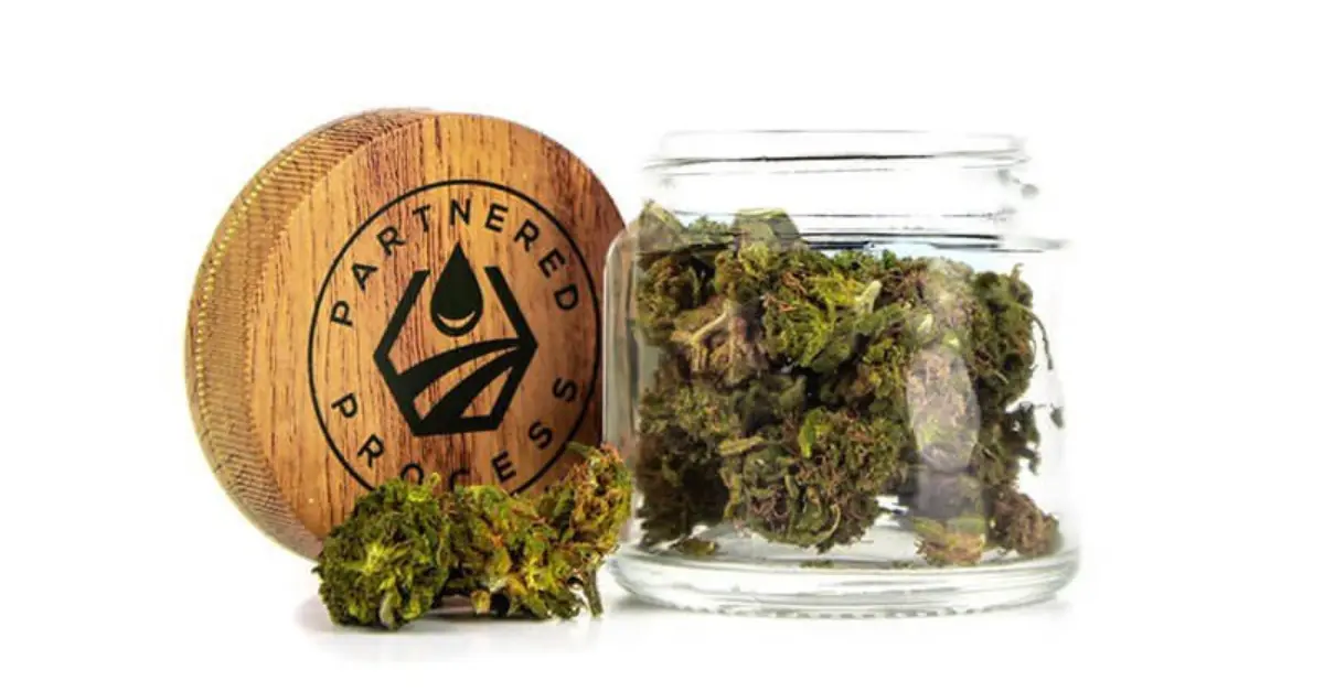 Smokable CBD products in glass jar beside wooden Partnered Process lid.