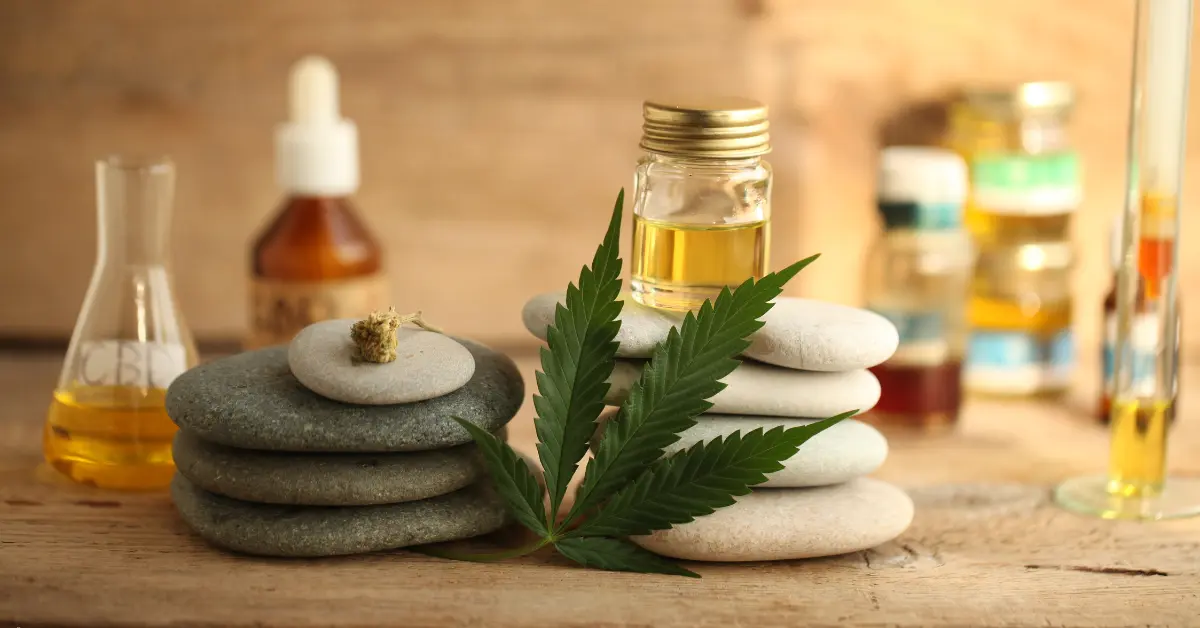 Topical CBD cream with essential oils and hemp leaf arranged beside spa stones for a natural wellness setting.