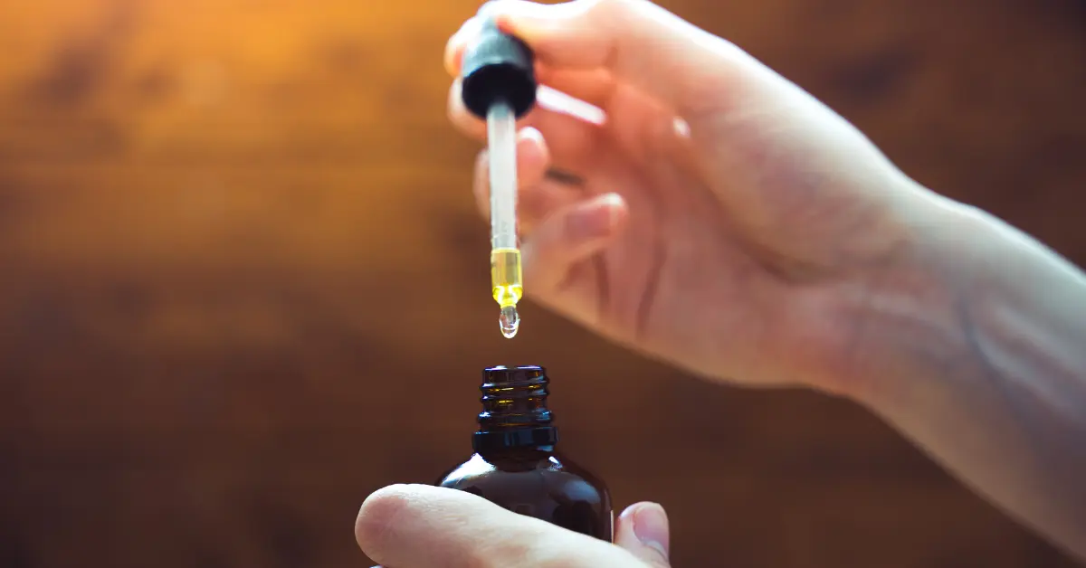 Topical CBD for pain relief being dispensed from a dropper into a brown glass bottle by hand.